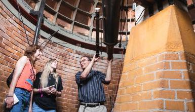 Mandi Laib (on right) and Isabel Henson speak with Dr. David Clevette in Doane's Boswell Observatory during a tour of the building on Stop Day 2023. 